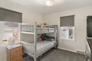 Bedroom with baseboards, visible vents, a textured ceiling, and dark carpet