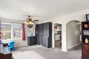 Interior space with ceiling fan, arched walkways, a textured ceiling, carpet floors, and baseboards