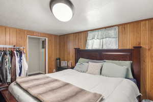 Bedroom featuring wooden walls, a closet, and a textured ceiling
