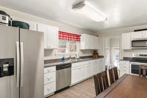 Kitchen featuring white cabinets, dark countertops, a sink, stainless steel appliances, and light wood finished floors