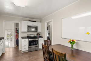 Kitchen with dark wood-style flooring, ornamental molding, white cabinetry, dark countertops, and stainless steel appliances