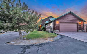 Cabin featuring log siding, driveway, a yard, and an attached garage