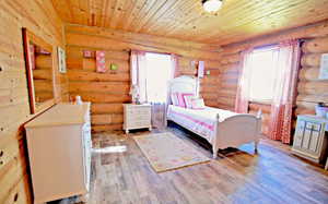 Bedroom with log walls, wooden ceiling, and wood pattern tile flooring