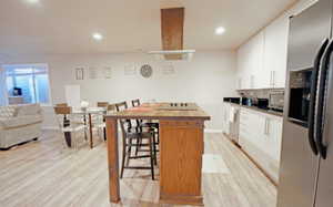 Basement kitchen with butcher block countertop island, recessed lighting, white cabinetry, appliances with stainless steel finishes, and light wood pattern floors