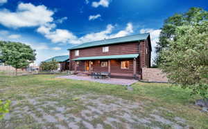 Back of property with metal roof, log siding, a patio area, and a lawn