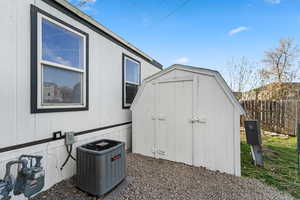 View of shed with central air condition unit and fence