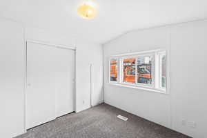 Unfurnished bedroom featuring visible vents, carpet flooring, vaulted ceiling, and a closet
