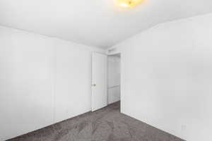 Carpeted empty room featuring visible vents and vaulted ceiling