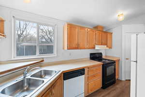 Kitchen featuring white appliances, under cabinet range hood, wood finished floors, light countertops, and a sink