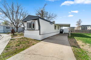 View of side of home with a yard, a carport, fence, concrete driveway, and an outbuilding