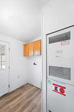 Clothes washing area with light wood-style floors, a textured ceiling, washer hookup, a heating unit, and cabinet space