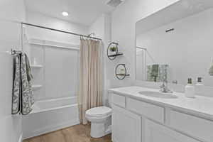 Bathroom with vanity, shower / tub combo with curtain, toilet, visible vents, and wood finished floors