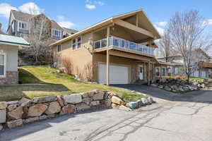 View of front facade with aphalt driveway, stucco siding, a front yard, a balcony, and a garage