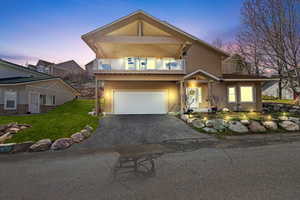 View of front facade with a balcony, stucco siding, aphalt driveway, a garage, and a lawn