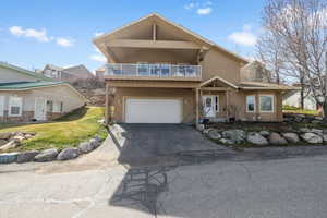 View of front facade with a balcony, stucco siding, driveway, a front yard, and a garage