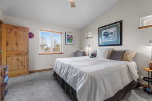Carpeted bedroom featuring ceiling fan, baseboards, and vaulted ceiling