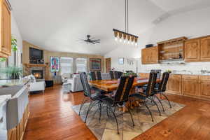 Dining area featuring a glass covered fireplace, high vaulted ceiling, hardwood / wood-style floors, and a ceiling fan
