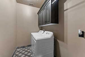 Washroom with baseboards, a textured ceiling, visible vents, cabinet space, and washer and dryer