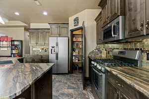 Kitchen featuring dark brown cabinets, visible vents, dark granite countertops, appliances with stainless steel finishes, and decorative backsplash