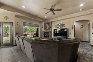 Living room with a fireplace, visible vents, a textured ceiling, and a ceiling fan