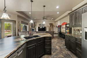 Kitchen featuring freestanding refrigerator, arched walkways, dishwasher, dark countertops, and a sink