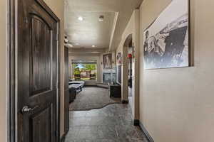 Hallway featuring baseboards, a textured ceiling, stone finish flooring, arched walkways, and carpet