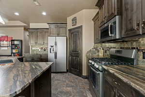 Kitchen with tasteful backsplash, dark brown cabinetry, dark granite countertops, visible vents, and stainless steel appliances