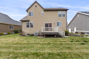 Back of house with a yard, a wooden deck, stucco siding, and central AC unit
