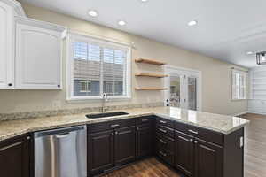 Kitchen with stainless steel dishwasher, dark wood-style flooring, white cabinets, and a sink