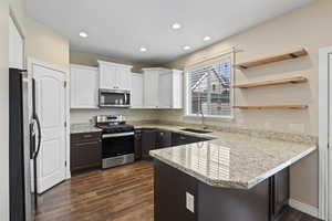 Kitchen featuring a peninsula, white cabinets, a sink, stainless steel appliances, and dark wood-style floors