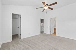 Unfurnished bedroom featuring a spacious closet, light colored carpet, vaulted ceiling, and baseboards