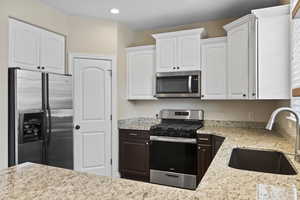 Kitchen featuring light stone counters, recessed lighting, white cabinetry, stainless steel appliances, and a sink