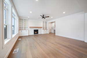 Unfurnished living room featuring light wood finished floors, visible vents, a lit fireplace, and ceiling fan