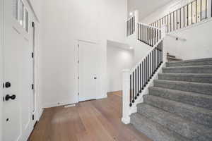 Foyer entrance featuring a towering ceiling, visible vents, wood finished floors, stairs, and baseboards