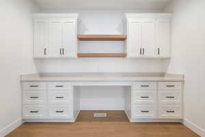 Unfurnished office featuring visible vents, built in study area, light wood finished floors, and baseboards