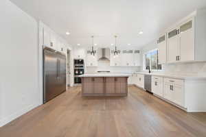 Kitchen with wall chimney range hood, built in appliances, a center island, and backsplash