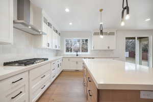 Kitchen featuring wall chimney exhaust hood, a kitchen island, light wood-style flooring, stainless steel gas cooktop, and decorative backsplash