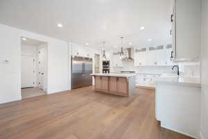 Kitchen with built in appliances, a sink, wall chimney range hood, light wood-style floors, and a kitchen island