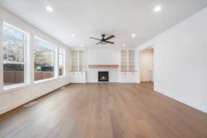 Unfurnished living room featuring baseboards, a warm lit fireplace, light wood-style floors, visible vents, and ceiling fan