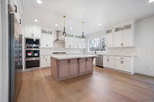 Kitchen with white cabinets, wall chimney exhaust hood, light countertops, light wood-style floors, and stainless steel appliances