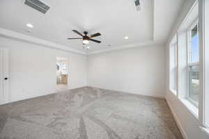 Carpeted empty room with plenty of natural light, visible vents, ceiling fan, and a raised ceiling