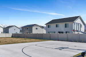 View of basketball court featuring a yard, basketball hoop, fence, and a residential view