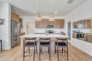 Kitchen featuring visible vents, light countertops, a kitchen island with sink, light wood-style floors, and stainless steel appliances