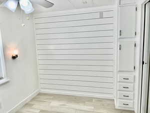 Room details with wood finished floors, wood walls, baseboards, and a ceiling fan