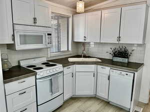 Kitchen featuring tasteful backsplash, white cabinets, a sink, light wood-type flooring, and white appliances