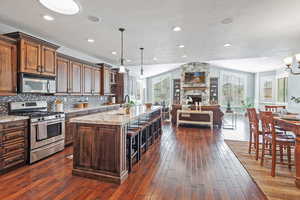 Kitchen with wood flooring, light granite counters, open floor plan, decorative backsplash, and stainless steel appliances