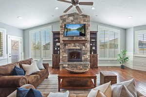 Living room with a stone fireplace, recessed lighting, wood floors, lofted ceiling, and ceiling fan