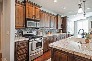 Kitchen featuring appliances with stainless steel finishes, light stone counters, a sink, decorative light fixtures, and decorative backsplash