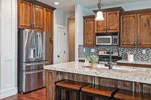 Kitchen featuring decorative backsplash, appliances with stainless steel finishes, and light stone counters