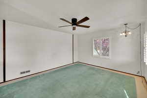 Spare room with carpet, visible vents, and ceiling fan with notable chandelier